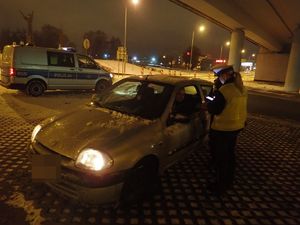 Policjantka ruchu drogowego w umundurowaniu, kontrolująca pojazd i jego kierowce, w ręku trzyma urządzenie do sprawdzania danych