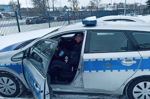 na zdjęciu policjant siedzi w radiowozie na siedzeniu kierowcy
