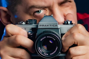 na zdjęciu Aleksander Van trzymający przy twarzy aparat fotograficzny