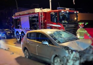 na zdjęciu samochód koloru srebrnego marki Peugeot na miejscu wypadku - w tle widać policjantów i wozy strażackie
