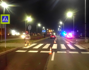 na zdjęciu miejsce wypadku drogowego - przejście dla pieszych, za nim czerwony samochód i pojazdy służbowe na sygnałach świetlnych stojące na drodze
