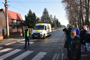 na zdjęciu policjant w kamizelce odblaskowej zatrzymuje pojazdy, by uczniowie mogli bezpiecznie przejść po pasach