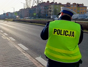 na zdjęciu policjant przy drodze mierzy prędkość przejeżdżającym pojazdom