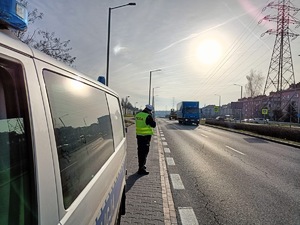 na zdjęciu policjant przy drodze mierzy prędkość przejeżdżającym pojazdom