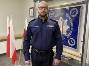 policjant w mundurze pozuje do zdjęcia na tle sztandaru komendy miejskiej w Częstochowie