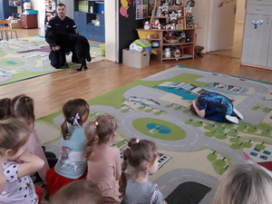 na zdjęciu policjant prezentuje dzieciom umiejętności psa służbowego