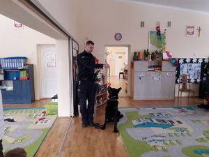 na zdjęciu policjant prezentuje dzieciom umiejętności psa służbowego