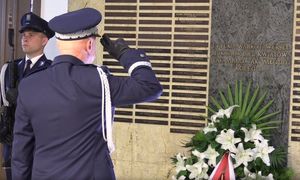 Policjant stoi przed tablicą i oddaje honor