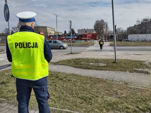 Policjant nadzoruje przejście dla pieszych którym przechodzi kobieta