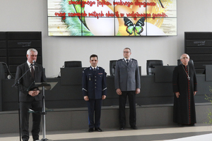 Mężczyzna przemawia do mikrofonu-obok dwóch policjantów i biskup