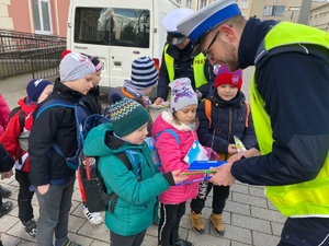 Policjant wręcza opaski odblaskowe dzieciom