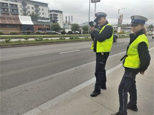 Policyjny patrol stoi przy drodze, jeden z nich miernikiem prędkości mierzy prędkość
