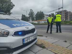 Policyjny patrol stoi przy drodze, obok stoi zaparkowany radiowóz