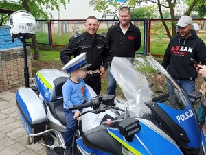 Dziecko w policyjnej czapce siedzi na policyjnym motocyklu-obok stoją policjanci