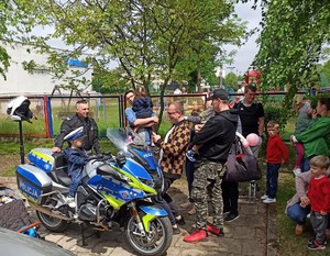 Uczestnicy pikniku stoją przy policyjnych motocyklach. Na jednym z nich siedzi przedszkolak w policyjnej czapce