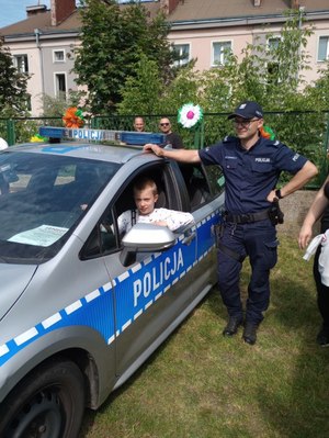 Chłopczyk siedzi za kierownicą radiowozu- obok pojazdu stoi umundurowany policjant