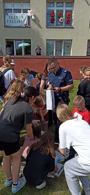 Policjant otoczony dziećmi na placu przedszkola wręcza im breloki