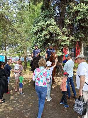 Dzieci i dorośli stoją przy koniach i niektóre z nich wyciągają ręce w kierunku koni