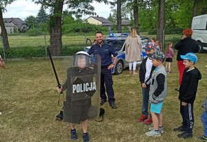 Policjant pozuje z chłopce ubranym z policyjny sprzęt- w tle stoi zaparkowany radiowóz