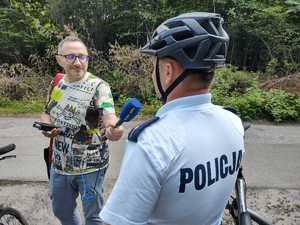 Policjant stoi przy rowerze i udziela wywiadu dziennikarzowi