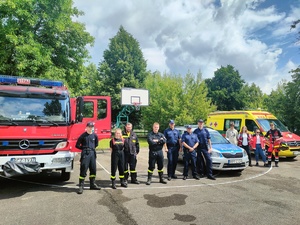 Wspólne zdjęcie policjantów, strażaków i ratowników medycznych na tle ich pojazdów służbowych