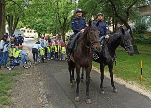 Policjanci na koniach przygotowani do rajdu rowerowego przedszkolaków, które ustawiają się do startu