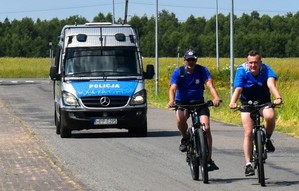 Dwaj rowerzyści przemierzają trasę, za nimi jedzie radiowóz