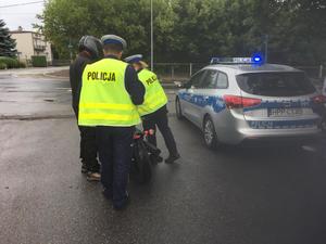 Policjanci w mundurach stoją przy radiowozie i rozmawiają z rowerzystą