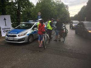 Rowerzyści rozmawiają z policjantami, którzy stoją przy drodze, obok zaparkowany radiowóz