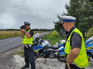 Policyjny patrol podczas działań na drodze stoi przy służbowych motocyklach- jeden z policjantów trzyma miernik prędkości