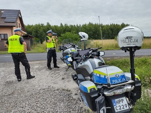 Policjanci na drodze kontrolują ruch pojazdów a za nimi dwa motocykle służbowe