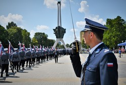 Na pierwszym planie dowódca uroczystości w mundurze galowym patrzący w stronę równo ustawionych na placu apelowym policjantów.