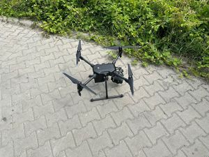 Policyjny dron znajdujący się na kostce brukowej obok trawnika.