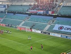 Widok z trybun na stadion w trakcie rozgrywanego meczu piłki nożnej.