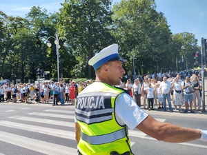 Policjant przy przejściu dla pieszych kieruje ruchem unosząc prawą rękę