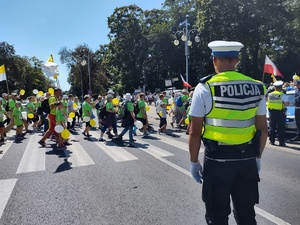 Policjant stoi na drodze i czuwa nad bezpieczeństwem pieszych, którzy przechodzą po pasach