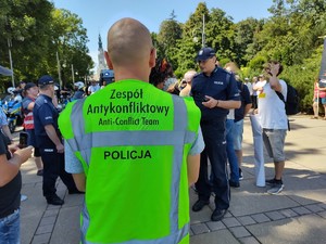 Policjant w kamizelce czuwa nad bezpieczeństwem zgromadzonych na dziedzińcu obywateli