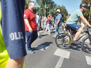 Rękaw policyjnej koszuli na tle pielgrzymów przechodzących przeze jzdnię