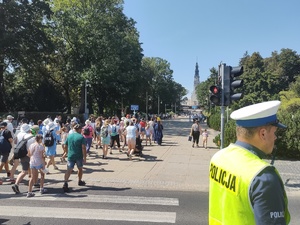 Policjant stoi na drodze i dba o bezpieczny przemarsz pielgrzymów