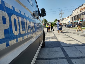 Policjanci rozmawiają z przechodniami w tle policyjny radiowóz