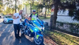 Chłopczyk siedzi na policyjnym motocyklu, obok stoi policjant i mężczyzna