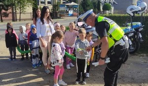 Policjant na drodze wręcza odblaski małym uczniom