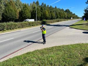 Policjant stoi przy drodze i mierzy prędkość pojazdów