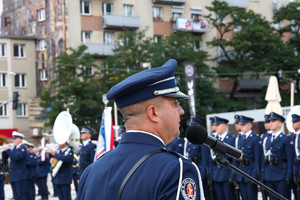 Policjant na tle zgromadzonych mundurowych zwrócony w ich kierunku