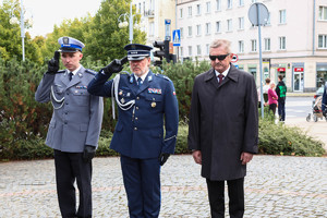 Delegacja 2 policjantów i innego mężczyzny oddaje honor przed pomnikiem