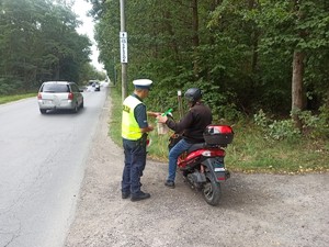 Policjant rozmawia z cyklistą, któremu przekazuje drobne upominki