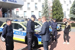 Policjant stoi przy radiowozie i  odbiera kluczyki od jednego z zaproszonych gości