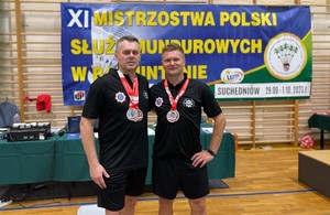 Dwaj policjanci w strojach sportowych z medalami pozują do zdjęcia