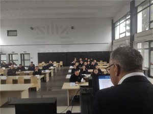 Mężczyzna mówi do mikrofonu, policjanci w mundurach służbowych siedzą w ławkach i słuchają wykładu