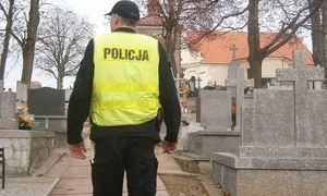 Policjant stoi przed ogrodzeniem cmentarza